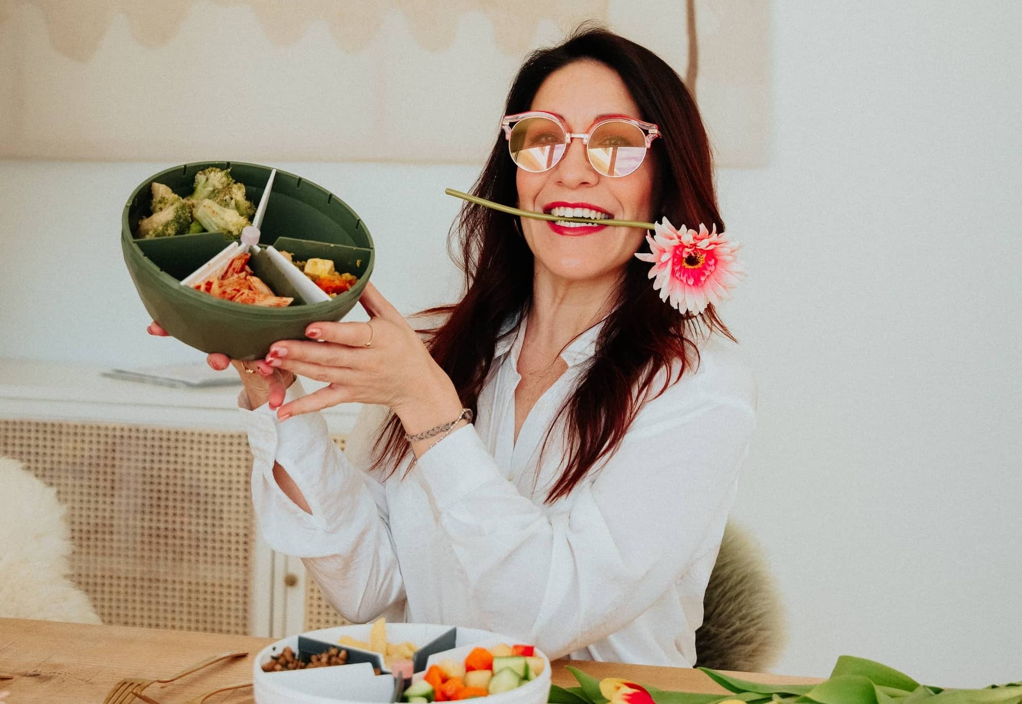 Femme avec des lunettes et des fleurs dans la bouche présente le bol maju de couleur kaki.