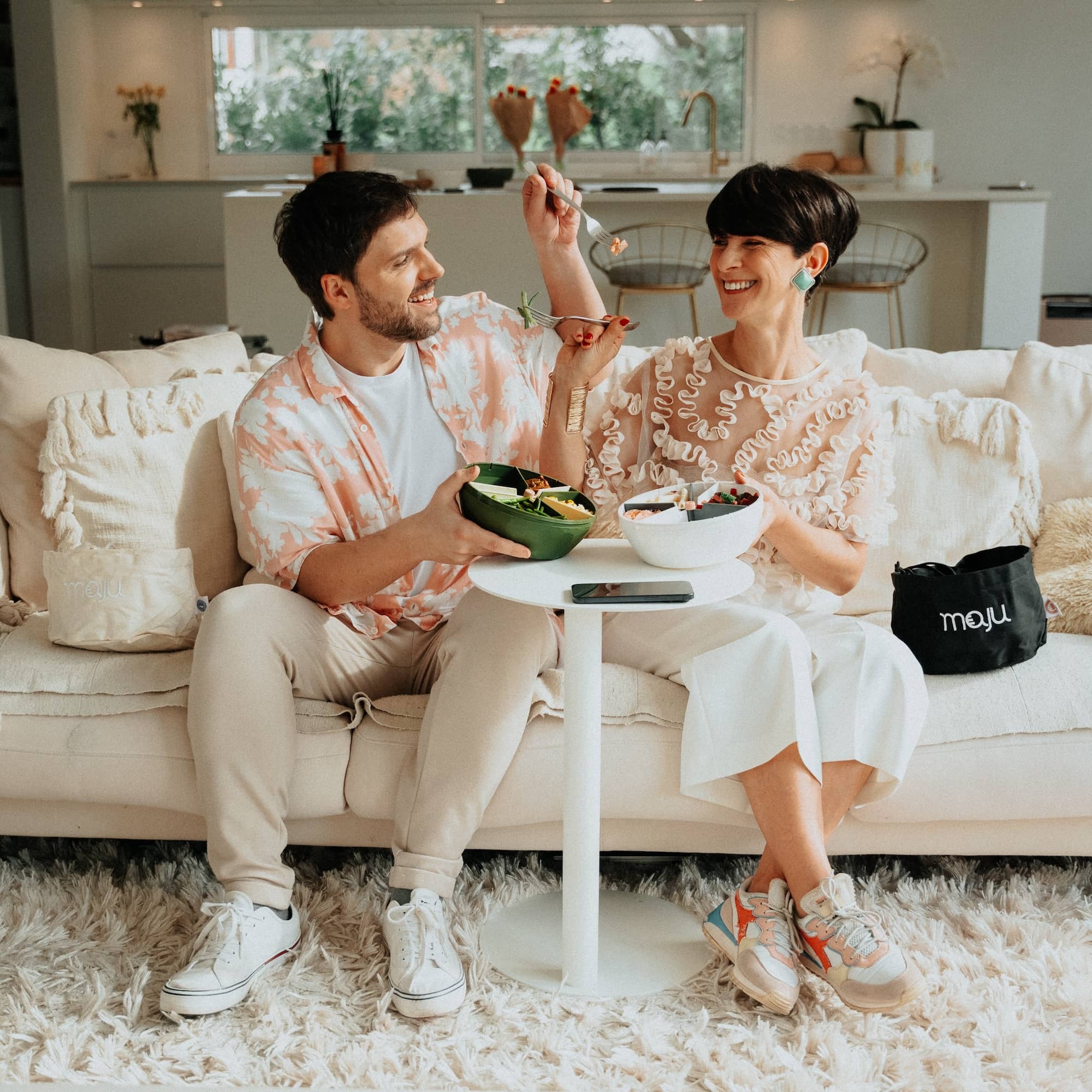 Couple qui se donnent à manger en souriant avec deux bols maju de couleur kaki et blanc.