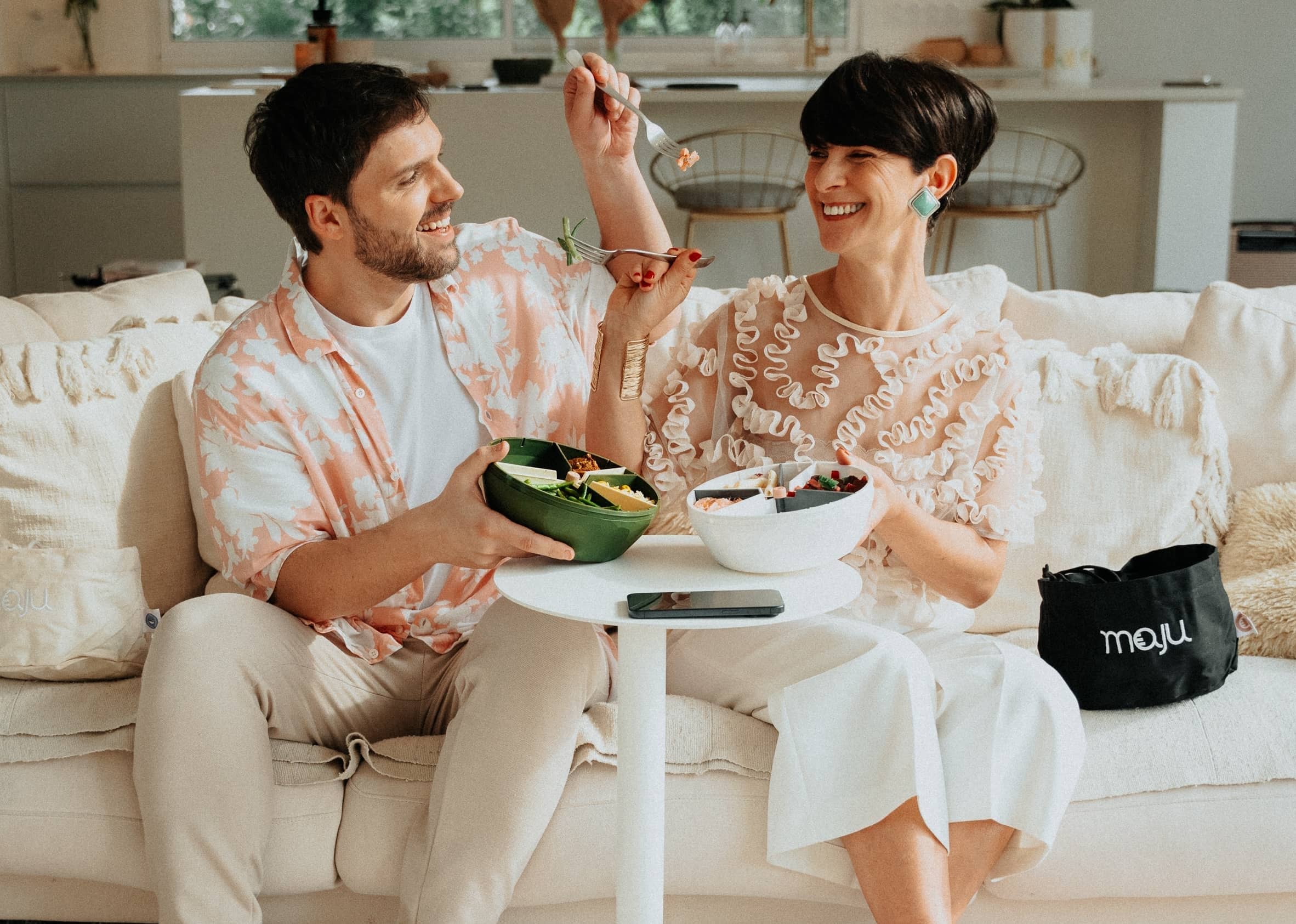 Couple qui se donnent à manger en souriant avec deux bols maju de couleur kaki et blanc.