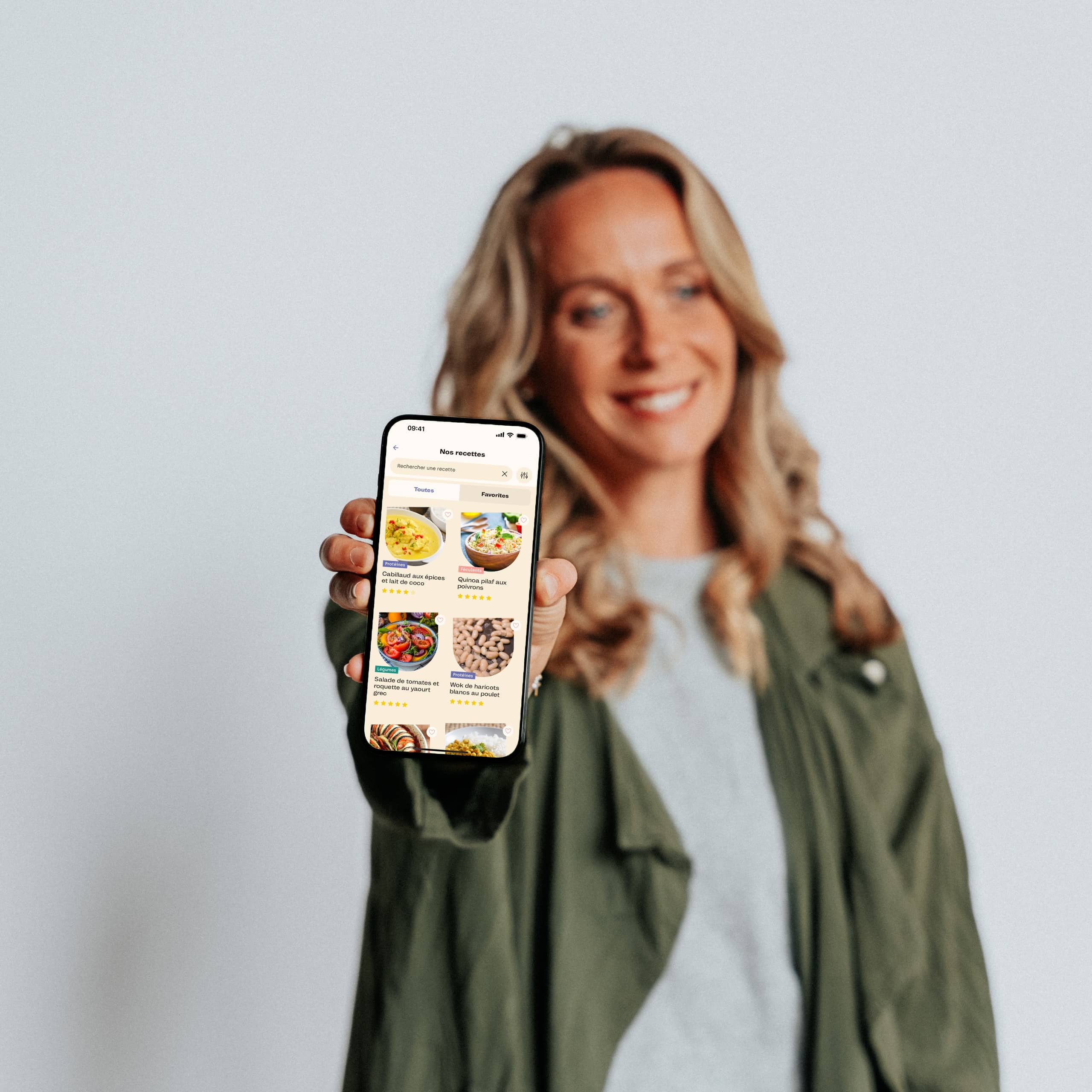 Femme blonde qui sourit en tenant un téléphone qui montre les recettes sur l'application maju.